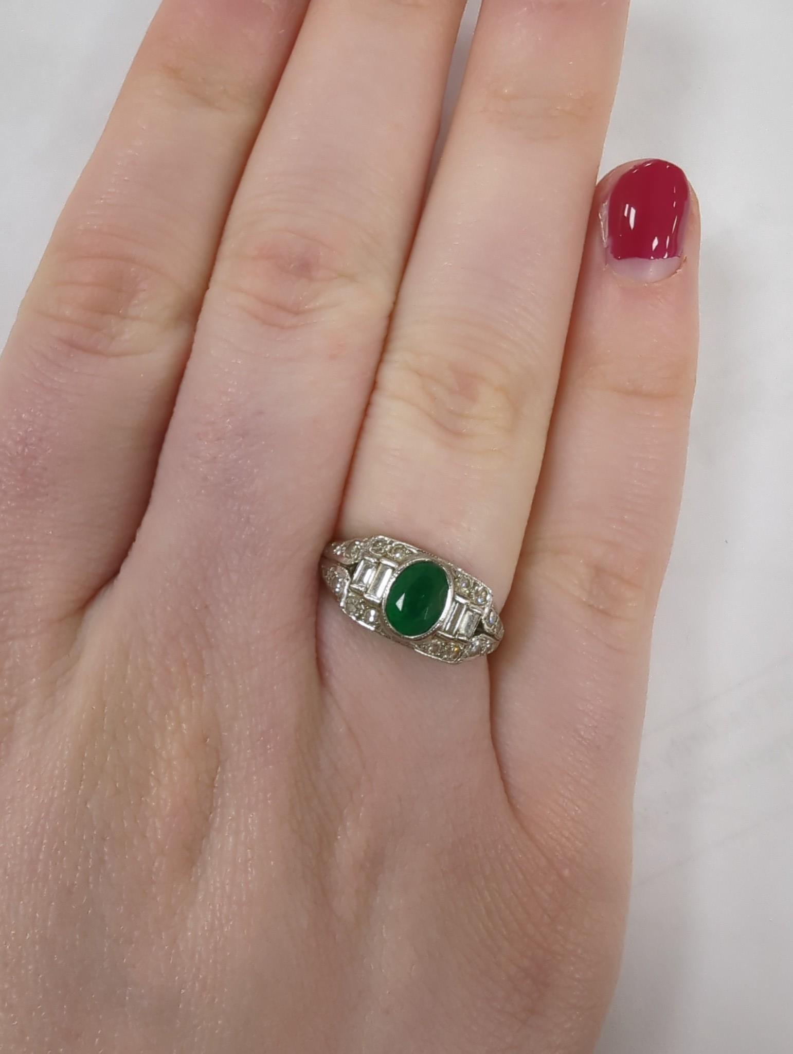 An Art Deco white metal, singe stone oval cut emerald and round and baguette cut diamond cluster set ring, size O/P, gross weight 4.2 grams.